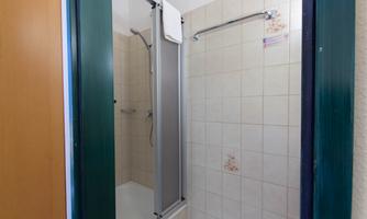 A simple bathroom with a shower cubicle and light tiles. The shower is equipped with a towel and a shower rod.