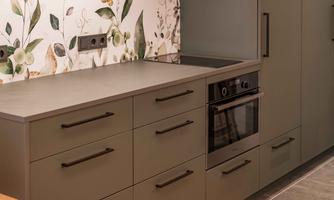 A modern kitchen with gray furniture and an integrated stove. The wall is designed with a decorative plant pattern.