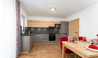 A modern kitchen with wood and gray furniture. The dining area is cheerfully decorated with red patterned napkins and a large table.