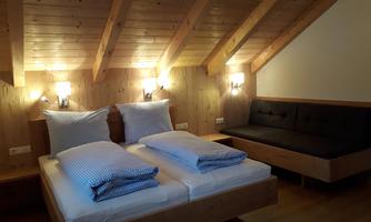 A cozy room with wooden walls and slightly sloped ceilings. There are two single beds and a sofa that invites relaxation.