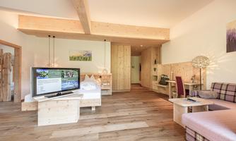 A modern room with wooden ceilings and furniture. There is a television, a bed, and a cozy seating area.