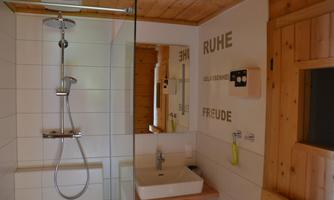 A modern bathroom with a shower and a sink. The walls are partially clad in wood and decorated with inspiring words.