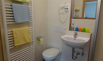 A modern bathroom with towels in soft colors. There is a sink, a toilet, and a towel rack.