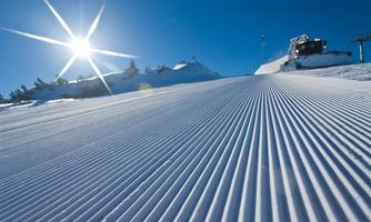 A groomed slope in the snow under a bright blue sky. The sun sparkles over the wintry ski area.