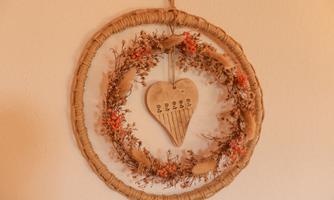 A decorative wall wreath made of dried flowers and plants. In the center hangs a heart-shaped wooden pendant.