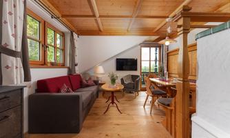 A cozy living room with wooden floors and wood paneling. There is a gray sofa, a table, and large windows with a view outside.