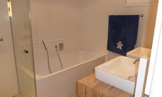 A modern bathroom with a freestanding bathtub and a separate shower. The decor is bright and simple, featuring a wooden vanity and a blue towel.
