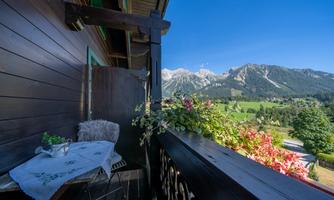 A beautiful balcony overlooking the mountains and a green landscape. Colorful flowers and a cozy seating area invite you to relax.