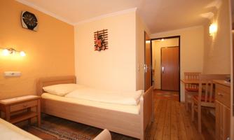 A simple room with two single beds and warm, orange walls. There is a table, chairs, and a door leading to another room.