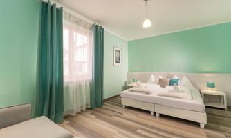 A bright bedroom with mint green walls and large windows. There is a cozy bed and soft lighting accents.