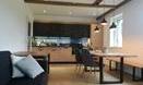 A modern living room with an open kitchen. There is a dining table and a cozy couch.