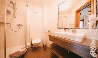 A modern bathroom with a shower and a double sink. The warm colors and bright light create an inviting atmosphere.
