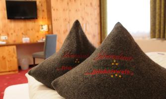 Two decorative cushions with embroidery in a cozy hotel room. In the background, a television and a desk are visible.