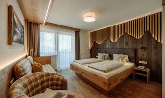 A modern bedroom with wooden elements and a cozy sofa. Large windows provide plenty of daylight and the atmosphere is inviting.