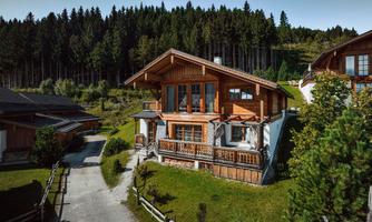 A charming wooden house nestled among green forests. The clear sky and surrounding nature create an inviting atmosphere.
