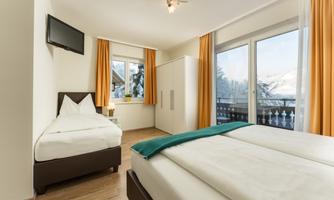 A bright and cozy bedroom with two beds and a television. Large windows offer a view of the snowy landscape.