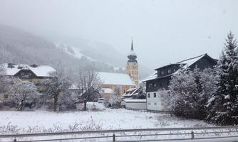 A snowy landscape with a small village and a historic church in the background. The surroundings are characterized by a calm winter atmosphere.