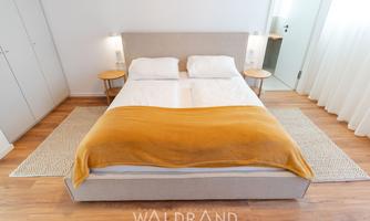A modern bedroom with a double bed and a bright yellow blanket. The floor is equipped with a light carpet and wooden surfaces.