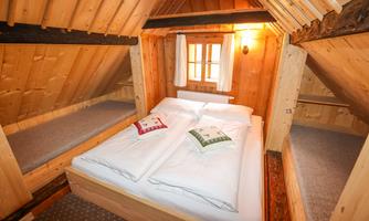 A cozy attic room with a double bed and wooden paneling. There are two small sleeping spots and a window that provides natural lighting.