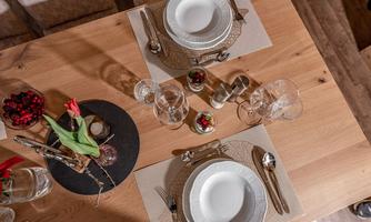 An elegantly set table with white plates, glasses, and cutlery. A floral decoration and fresh fruit complete the arrangement.