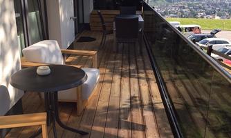 A cozy balcony with a wooden floor and modern furniture. In the background, a beautiful mountain landscape stretches out.