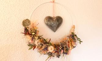 A decorative wall wreath made of dried flowers and grasses. In the center hangs a heart-shaped metal object.