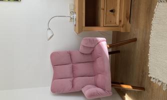 A cozy, pink armchair is next to a wooden table with a lamp. The floor is covered with a light carpet.