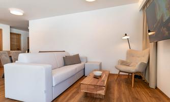 A modern living room with a white sofa and a wooden coffee table. Next to the sofa is a comfortable armchair and a floor lamp.
