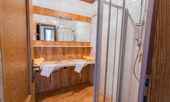 A bright bathroom with wooden paneling and modern fixtures. The shower is separated by glass walls, and fresh towels are ready.