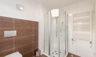 A modern bathroom with a glass shower. The walls are in light and brown tones.