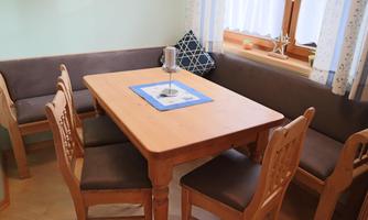 A cozy dining area with a wooden table and chairs. Against the wall, there is a comfortable bench and a decorative table with a candle holder.