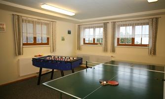 A bright room with foosball and a table for table tennis. The windows are decorated with curtains and let in a lot of daylight.
