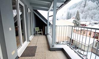 A balcony with a chair, surrounded by snow-covered mountains. The atmosphere is calm and inviting.