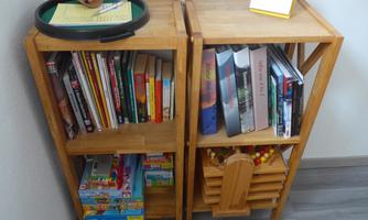 A wooden shelf with many books and magazines. On the top shelf, there is a tray with a note and a calendar.