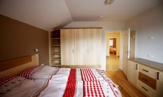 A cozy bedroom with a double bed and a wooden wardrobe. The room has painted walls and a warm, inviting style.