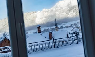 A winter landscape with snow-covered roofs and mountains in the background. The view shows a clear sky and a picturesque view of the village.