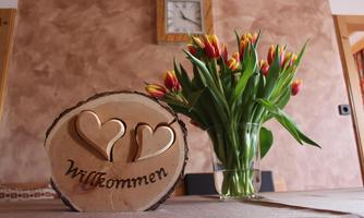 A warm welcome sign made of wood with two hearts stands in the foreground. In the background, you can see a beautiful bouquet of tulips.