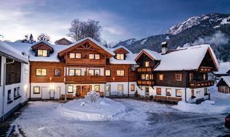 A cozy vacation home in the snow with a traditional alpine style. The surroundings are picturesque, surrounded by mountains and a serene winter landscape.