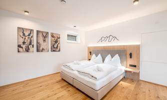 A modern bedroom with a double bed and two decorative pillows. Pictures of animals hang on the walls, and the floor is made of wood.