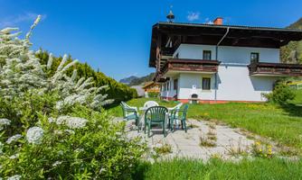A cozy holiday house with balconies and surrounding greenery. Garden furniture is on a terrace at the edge of the garden.