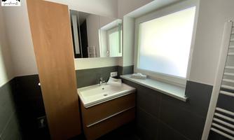 A modern bathroom with a white vanity and wooden cabinets. The window provides plenty of natural light.