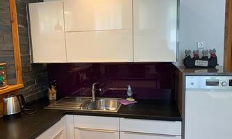 Modern kitchen with white cabinets and a purple backsplash. The stainless steel sink and dishwasher are also visible.