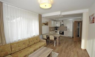 A modern living room with a cozy couch and a dining table. The open kitchen is bright and well-equipped.
