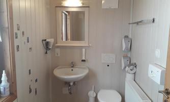 A simple bathroom with a sink, a toilet, and a mirror. The walls are light, and there are some towel holders.