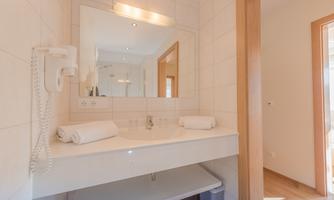 A modern bathroom with a sink and a large mirror. Two clean towels are on the shelf.
