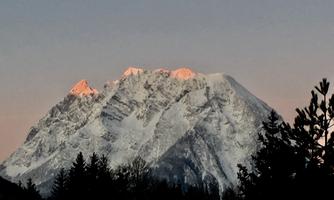An impressive mountain with snow-covered peaks and a gentle morning light. Surrounding trees enhance the majestic atmosphere.