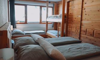 A cozy room with wooden walls and several beds. Large windows provide plenty of natural light.