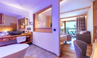 A modern bathroom with a freestanding bathtub and bright wooden details. The room has a cozy atmosphere and a view of the balcony with seating.