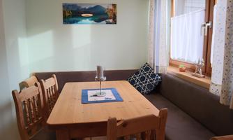 A cozy dining area with a wooden table and benches. The window offers a view of nature and the room has a bright, inviting atmosphere.