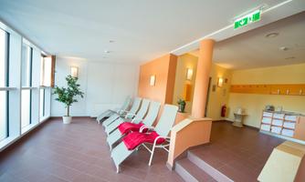 A bright relaxation room with loungers and a relaxing atmosphere. On one wall, there are plants and some practical facilities are visible.